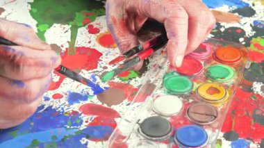 Sanatçının elleri, sanatta yaratıcı imgeler yaratmak için çalışır. Resim boyaları ve fırçalar, palet, guaj ve suluboya kullanarak tuvale çok renkli dokunuşlar uyguluyorlar..