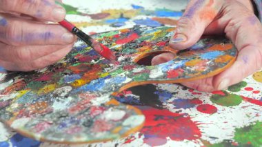 Sanatçının elleri, sanatta yaratıcı imgeler yaratmak için çalışır. Resim boyaları ve fırçalar, palet, guaj ve suluboya kullanarak tuvale çok renkli dokunuşlar uyguluyorlar..