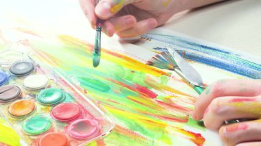 Sanatçının elleri, sanatta yaratıcı imgeler yaratmak için çalışır. Resim boyaları ve fırçalar, palet, guaj ve suluboya kullanarak tuvale çok renkli dokunuşlar uyguluyorlar..