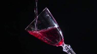 Kırmızı kuru şarap, şişeden bardağa dökülüyor, siyah arka planda. Yakın plan. Yavaş çekim.