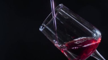 Kırmızı kuru şarap, şişeden bardağa dökülüyor, siyah arka planda. Yakın plan. Yavaş çekim.