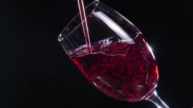 Kırmızı kuru şarap, şişeden bardağa dökülüyor, siyah arka planda. Yakın plan. Yavaş çekim.