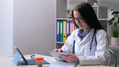 Genç doktor, doktorluk yapıyor, tıbbi ekipmanlarla çalışıyor, hastaların tıbbi geçmişlerini araştırıyor. Yavaş çekim.