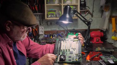 Yaşlı bir zanaatkar bir atölyede elektronik panoları tamir eder. Yavaş çekim.