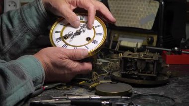 Klasik saat mekanizması. Eski bir ustanın elleri antika bir saati dikkatlice ayarlar ve hayata döndürür. Antikaların restorasyonu.