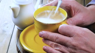 Yaşlı bir adam çay tabağında bir fincan espresso kahvesi tutuyor. Eller, yakın plan. Yavaş çekim.