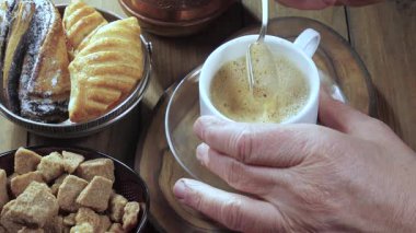 Yaşlı bir adamın elleri yavaşça sıcak espresso kahvesini kaşıkla karıştırıyor. Yavaş çekim.