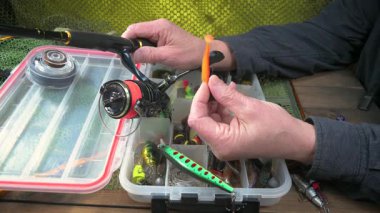 Yaşlı bir balıkçı balıkçı olta takımlarını toplayıp ekipmanları kontrol ediyor. Ellerine yakın çekim..