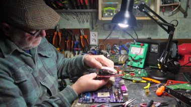 Atölyedeki ana kartı tamir et. Ustanın elleri, kullanım sürecindeki arızalar nedeniyle elektronik aletleri tamir edecek şekilde yakın plan çekimde. Yakın plan. Yavaş çekim.