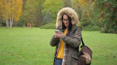 Genç, güzel bir kız doğada seyahat eder, sonbahar ormanının güzelliğine hayranlıkla hayran kalır, fotoğraf çeker, defterine notlar yazar, gülümser, eğlenir. Yavaş çekim.