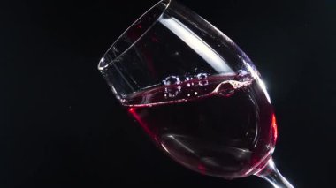 Kırmızı şarap kadehte yavaşça karıştırılıyor. Karanlık arka plan. Yavaş çekim.