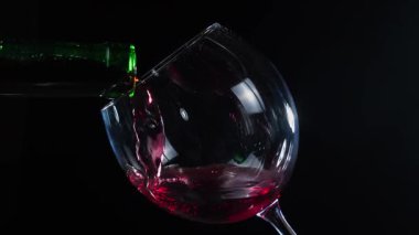 Kırmızı şarap bir bardağa koyu bir arka plana dökülüyor. Yavaş çekim.