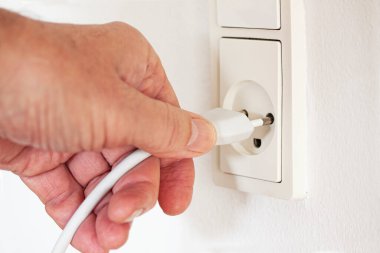 Duvardaki modern beyaz prizin kablosunu çekerken ya da çekerken elinizi kapatın. Beyaz bir arka planda elektrik prizine takılı bir elektrikli aletin fişi. Elektrik ve güç kavramı.