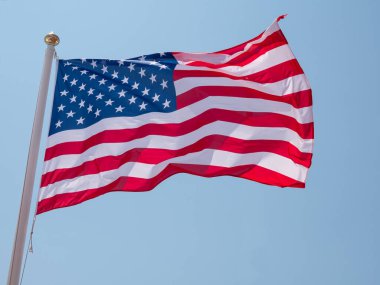 Yıldızlar ve Çizgiler, mavi gökyüzü arka planına sahip bir bayrak direğinde rüzgarda dalgalanan ABD bayrağı. Mavi gökyüzü arka planına sahip bayrak direğinde dalgalanan Amerikan Yıldızları ve Şeritleri.