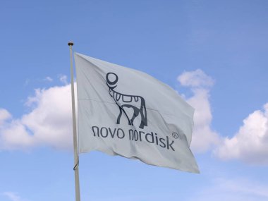 Novo Nordisk bayrağı mavi gökyüzü arkaplanlı bayrak direğinde dalgalanıyor. Merkezi Danimarka 'da olan bir ilaç firması. Kopenhag, Danimarka - 12 Ağustos 2023. 