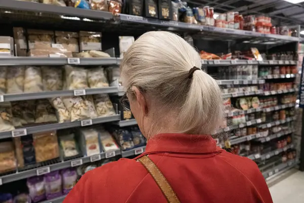 Woman shopping in food department of a supermarket. Close up of woman seen from behind  with blond hair and red sweatshirt.