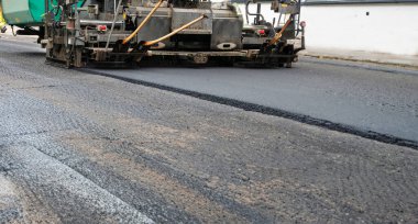 Asfalt yol yüzeyinin tamiri - eski katman kaldırıldı ve inşaat sahasına yeni asfalt döşeyen endüstriyel kaldırım kamyonu.