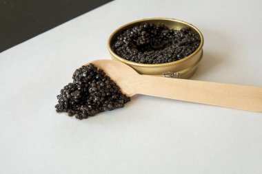 Beyaz arka planda kaşıkla açık bir teneke kutunun dışında siyah havyar. Gurme deniz ürünleri lezzeti..