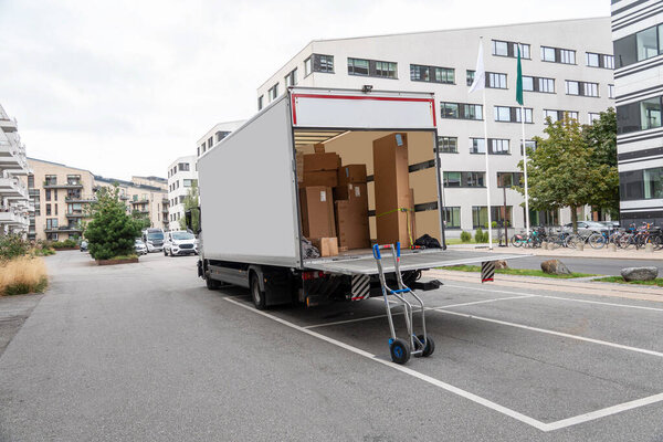 Белый грузовик с открытыми задними воротами перед офисным зданием. Копирование пространства.