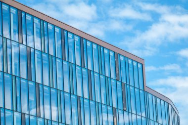 Mavi ve dağınık beyaz bulutlu modern minimalist cam bina pencerelere yansıyor. Kopenhag, Danimarka - 15 Mayıs 2025.