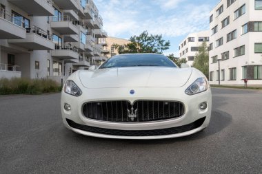 Beyaz Maserati spor araba ön manzara ön ızgara logosu Maserati mızraklı. Geniş açı, alçak açı, çekim. Modern apartman ve ofis binaları tarafından park edilmiş. Kopenhag, Danimarka - 14 Temmuz 2025.