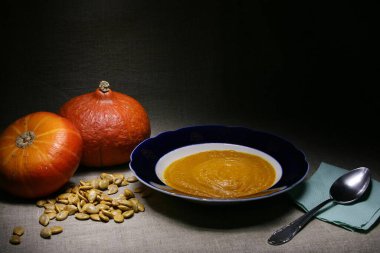 İki kırmızı Hokkaido balkabağı, beyaz tohumları ve gri keten üzerinde bir kase kabak püresi