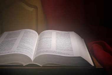 Harika bir ışık saçan açık bir İncil dekoratif bir kapıyı kaplayan kırmızı bir bezin arka planına karşı bir masanın üzerinde yatar.