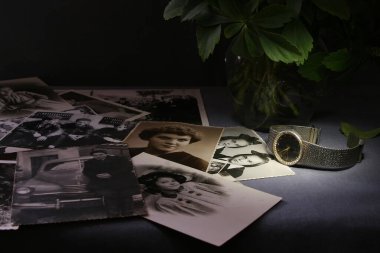 Eski fotoğraflar masanın üzerine saçılmış, ve onların yanında eski bir saat ve takılmış bir bilezik var..