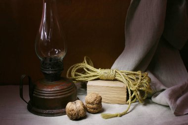 Masanın üzerinde eski soyulmuş bir gaz lambası, tahta bir blok ve sarı bir ip var..