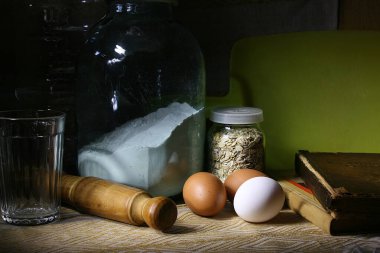 Masanın üzerinde ürünler var: un, yumurta, pullar ve yemek kitaplarıyla birlikte bir merdane.