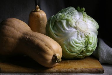 Yeni hasat zamanı beyaz lahana ve iki balkabağı kesme tahtasının üzerinde gri bir bez arka planda yatıyor..
