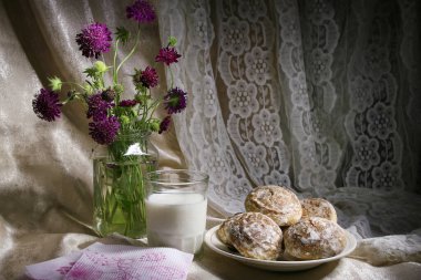 Sütlü zencefilli çörek. Masanın üzerinde zencefilli ekmek ve dantel kumaşların arka planında bir buket yabani çiçekle süslenmiş bir bardak süt var.