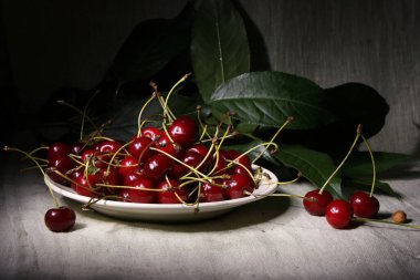 Kirazlarla dolu beyaz bir tabakta ve kiraz dallarında