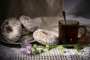 Yakın plan: zencefilli çörek halkaları ve şeffaf bir fincan çay, çiçekle süslenmiş.