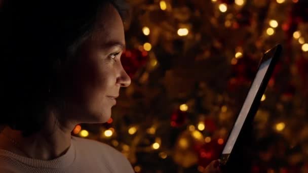 在圣诞背景下 使用数码平板水龙头在屏幕上对成年女性进行特写 圣诞彩灯闪烁 神奇的圣诞光彩夺目 — 图库视频影像