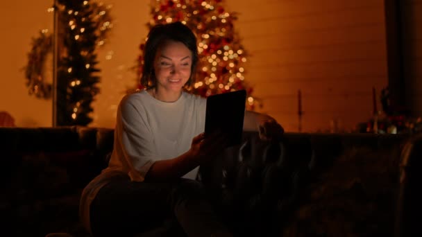 在圣诞节的背景下 成年女性与朋友或家人举行视频通话 在圣诞前夕举行平板电脑晚会 彩灯闪烁 魔幻夺目 — 图库视频影像
