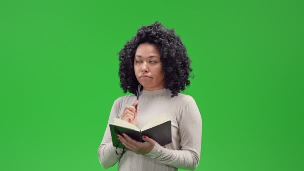 アフリカ系アメリカ人の女性思慮深い計画リストやショッピングリストを保持ノートブックとペンを行うには緑の画面に隔離 — ストック動画