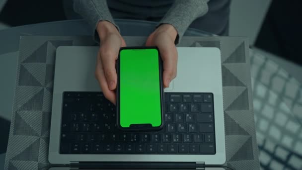 上图所示女性手持智能手机 桌上有绿色屏幕笔记本电脑 — 图库视频影像