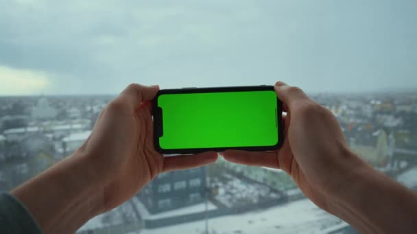 男子手持智能手机与绿色屏幕玩网络游戏装置从一边移动到另一边的背景冬季城市视图 — 图库视频影像