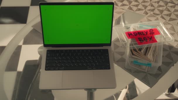 テーブルのノートパソコンに緑の画面のスマートフォンを使い将来の計画予算のために貯金箱を使う女性 — ストック動画