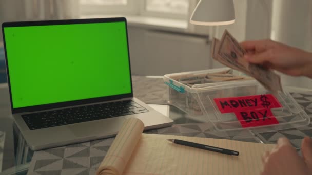 女性はノートパソコンにノートを書き緑の画面で学生ローンのための貯蓄金融クッションとお金をカウントします — ストック動画