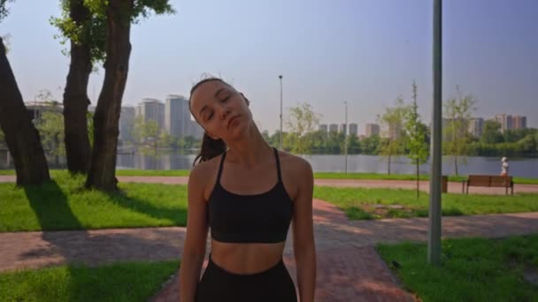 ランナーは ジョギング前に首のための暖かいアップエクササイズをしている夏の公園の女性で体を伸ばすアクティブウェアを着た — ストック動画