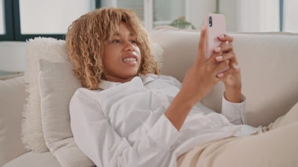 Женщина Лежит Диване Держа Руках Мобильный Телефон Выглядит Расслабленной Сосредоточенной — стоковое видео