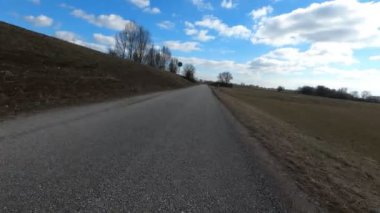 Mavi bulutlu manzara ve mavi bir su kütlesinin yanındaki yeşil çayırlar.