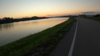 Mavi bulutlu manzara ve mavi bir su kütlesinin yanındaki yeşil çayırlar.