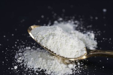 close up of a spoon with a pile of salt sugar and powdered.