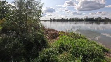 Yüzen göl, bulutların yansımalarıyla hafif bir rüzgar ve kıyıdaki bitki örtüsüyle