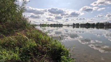 Yüzen göl, bulutların yansımalarıyla hafif bir rüzgar ve kıyıdaki bitki örtüsüyle