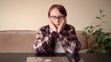 80 yaşında yaşlı bir kadın dizüstü bilgisayarı ve telefonuyla oturmuş çocuklarından telefon bekliyor..