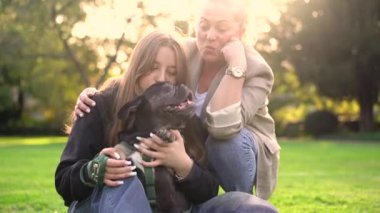 Anne ve kızı, köpekleri Fransız bulldog 'la parkta oynuyorlar. Çimlerin üzerinde 4K görüntüleri var.